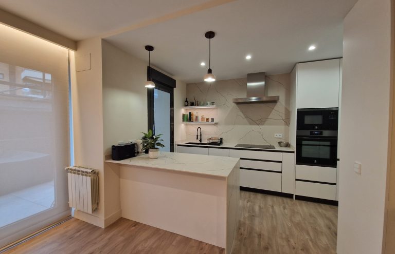 Cocina moderna blanca con isla y electrodomésticos integrados.