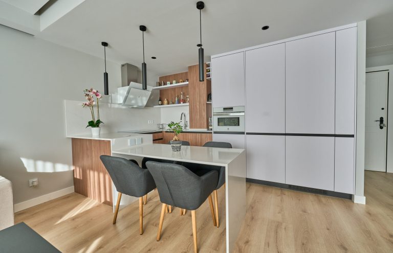 Cocina moderna blanca y madera con isla y taburetes.