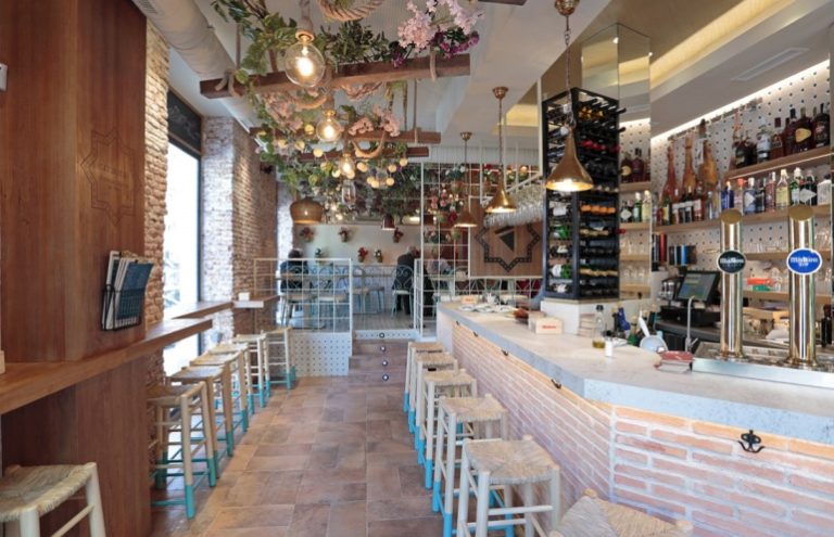 Bar interior con decoración floral y taburetes azules.
